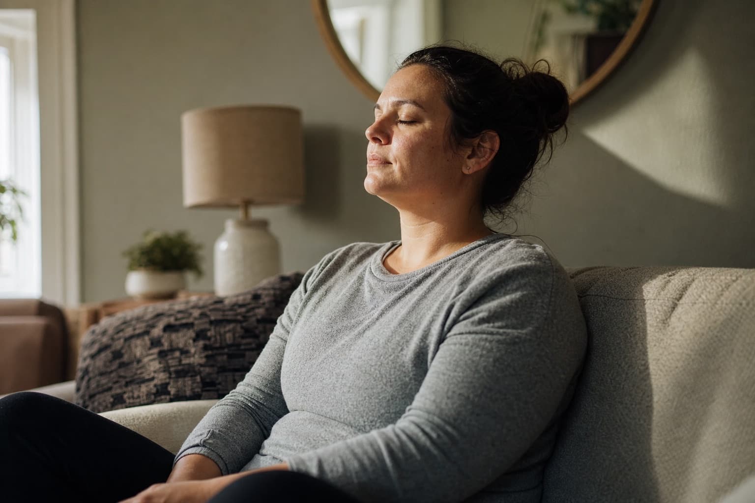 An adult resting calmly on a couch in a sunlit room during a quiet, mindful moment
